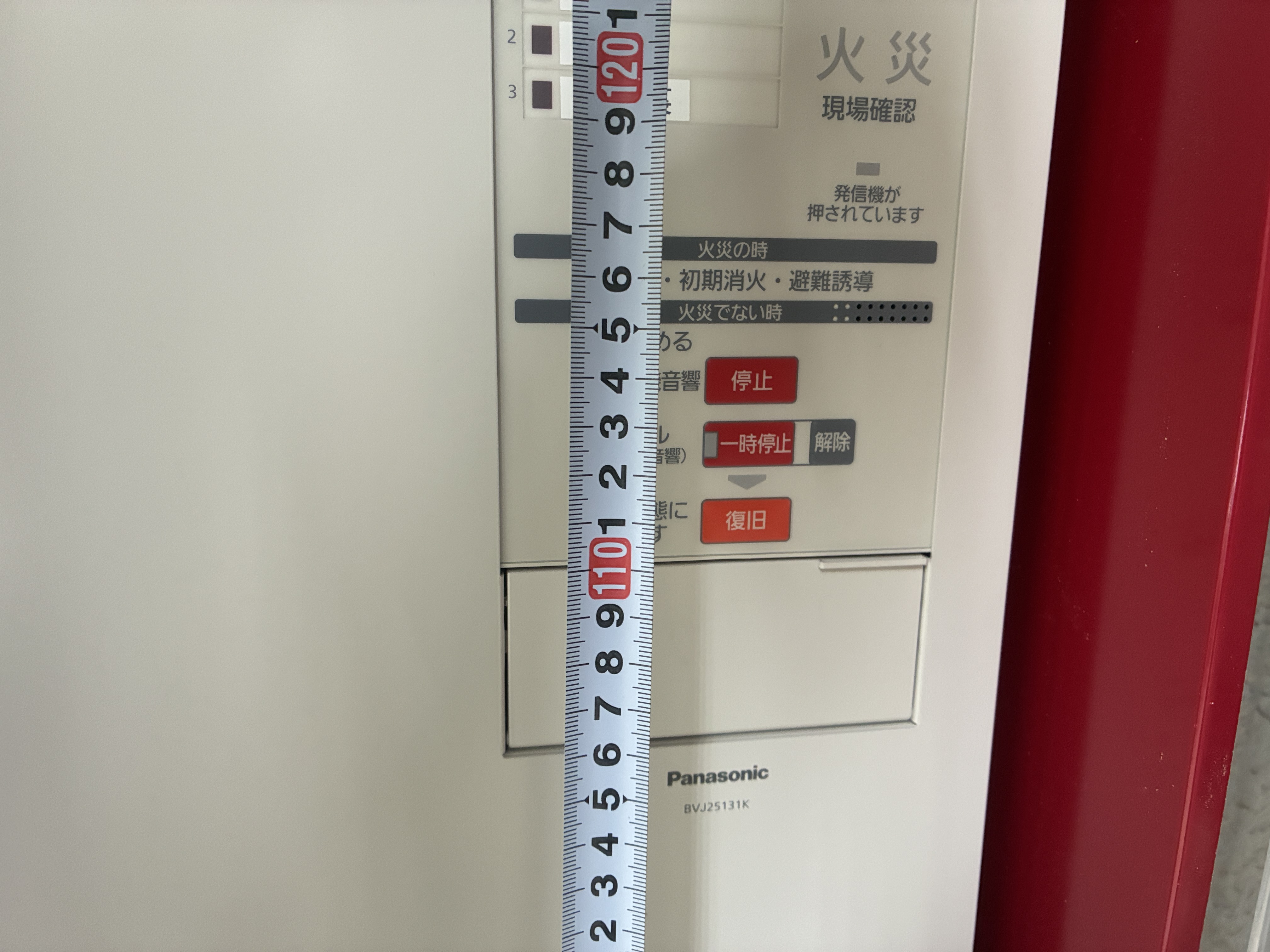 新しい火災受信機の操作部の高さをメジャーで計測。操作スイッチが床面から0.8m以上1.5m以下の範囲に収まることを確認