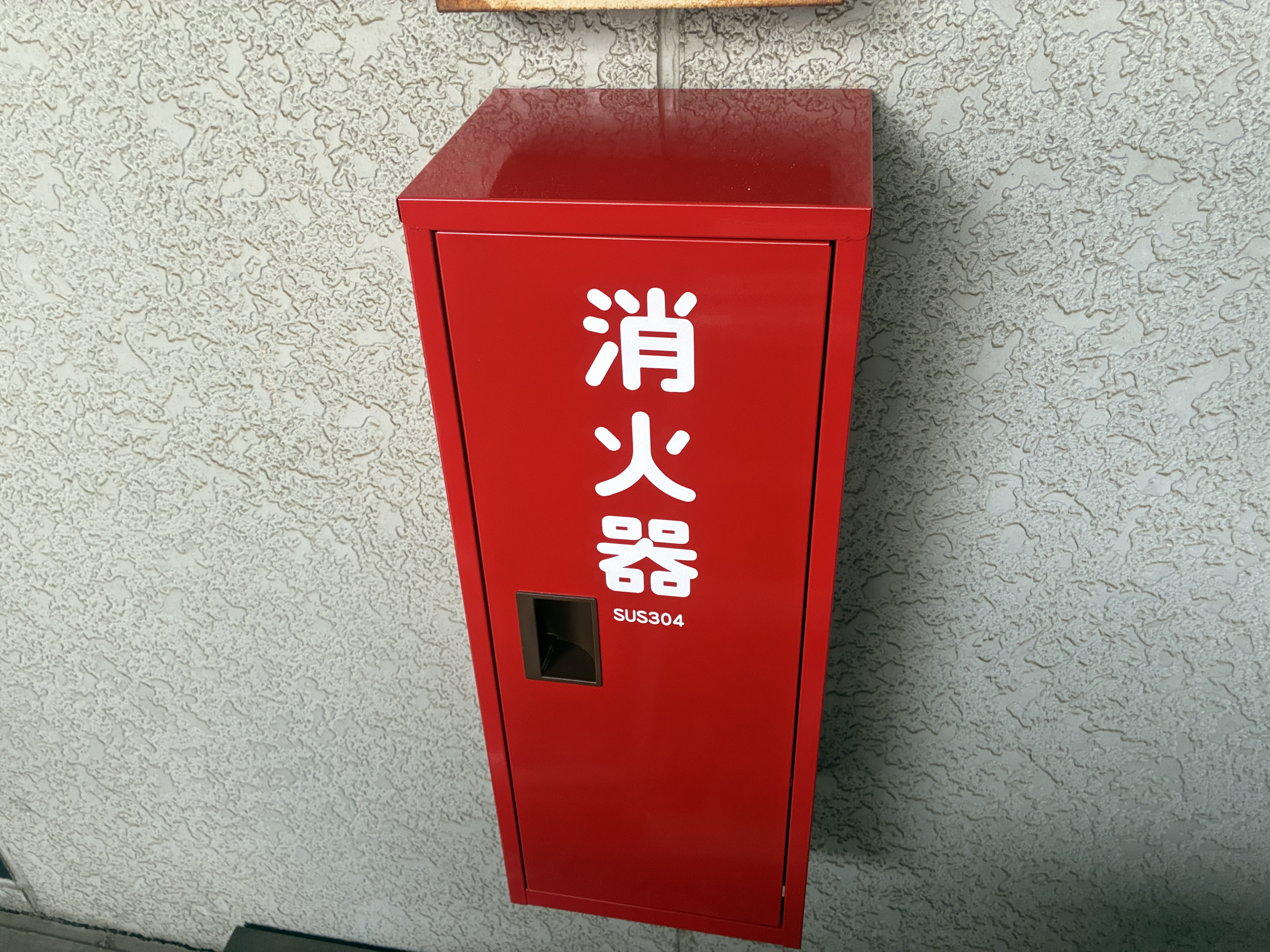 交換後のステンレス製（SUS304）消火器格納箱。赤い塗装仕上げで錆の心配がない