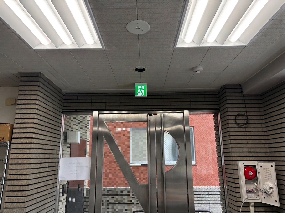 カフェ出入口の上部に設置したLED避難口誘導灯（C級片面型）と天井の光電式煙感知器
