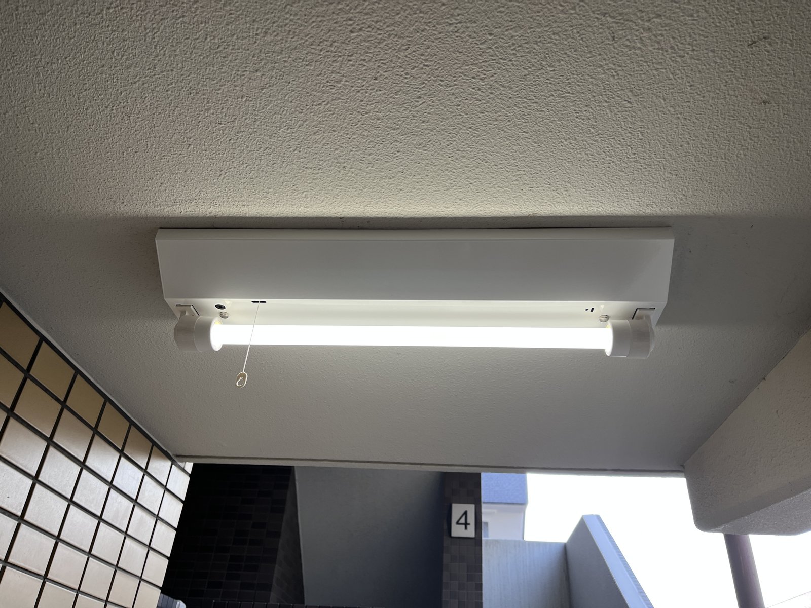 交換後のLED非常灯が開放廊下の天井で点灯している様子。白く均一な光で廊下を照らしている