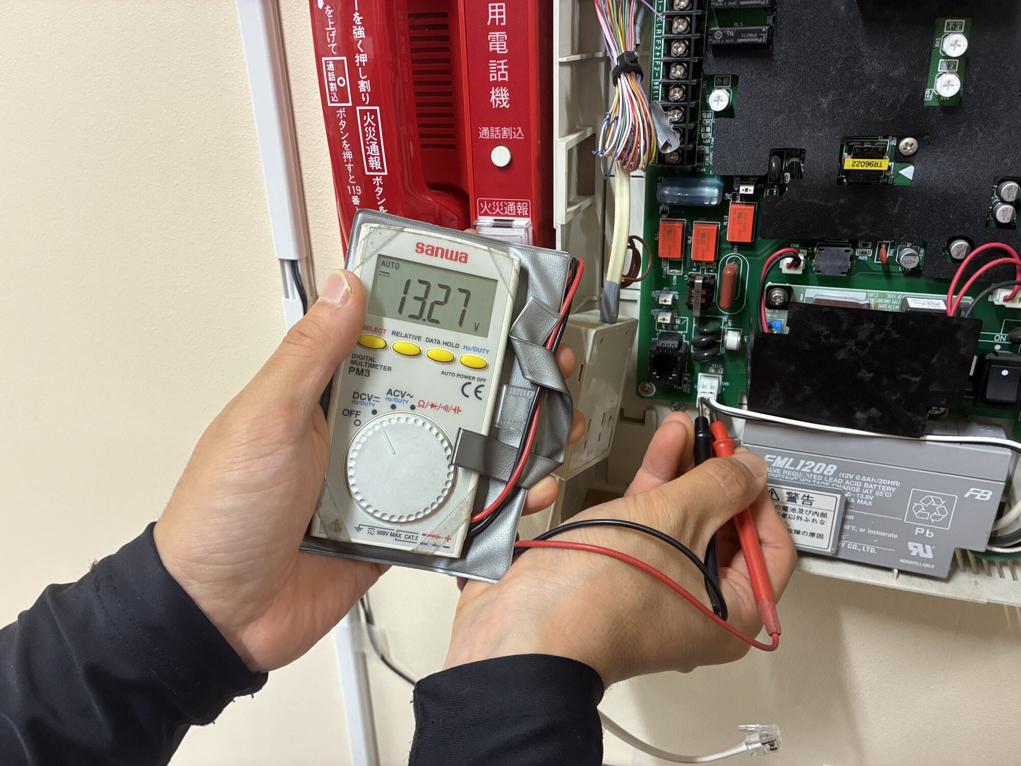 交換後のバッテリー電圧をテスターで測定している様子