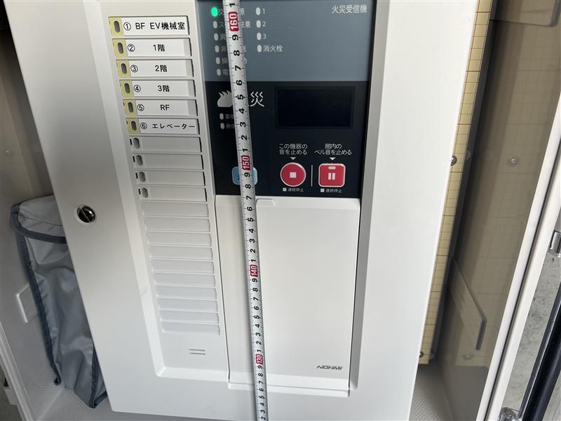 新しい火災受信機の操作部の設置高さをメジャーで確認している様子