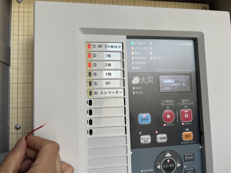 受信機の端子から共通線を引き抜き、断線表示が出ることを確認する試験の様子