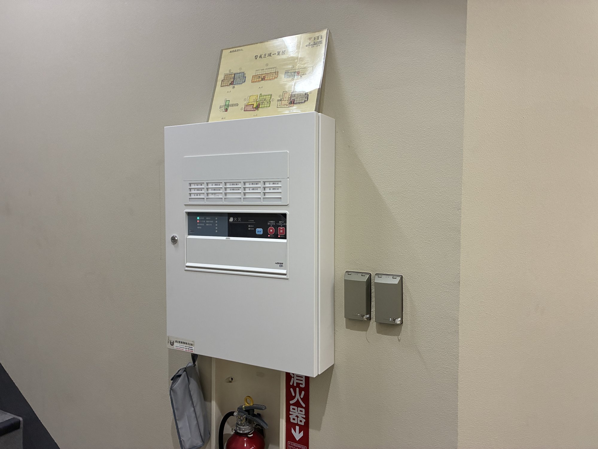 東京都新宿区の共同住宅に設置した交換後のP型1級火災受信機（自動試験機能付き）。上部に警戒区域一覧図を掲示