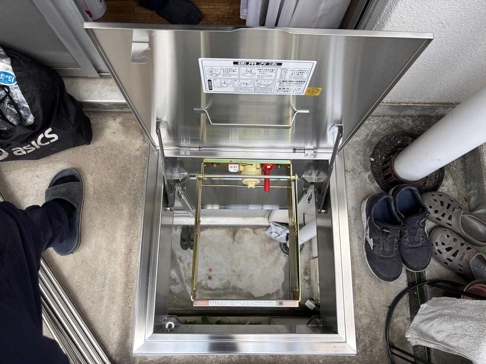 上蓋を全開にした交換後の避難ハッチ。上蓋の裏面に使用方法のステッカーが貼られ、展張レバーと危険防止ロックが見える