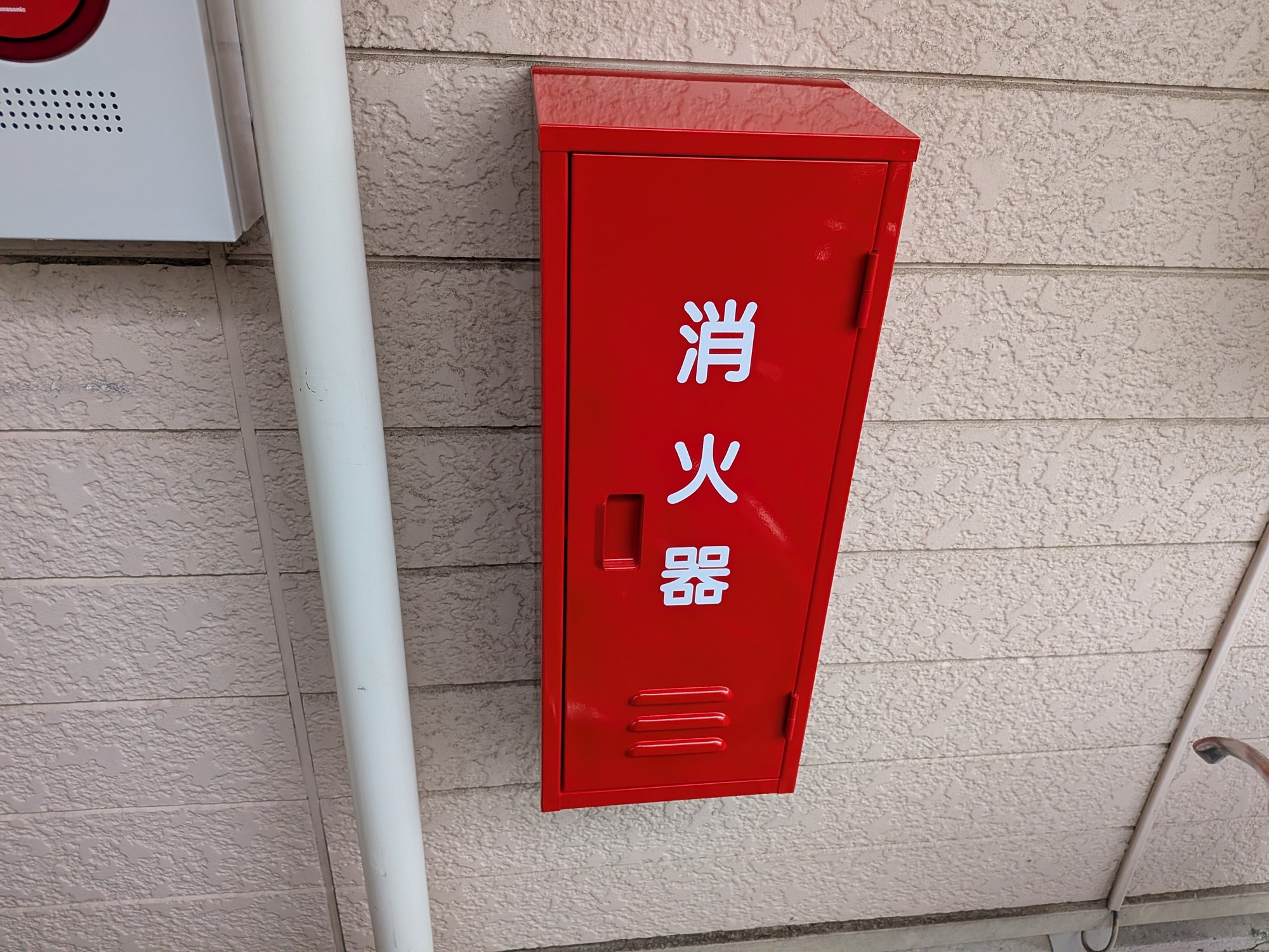 交換後の赤い消火器格納箱。外壁に新しく取り付けられ、白い「消火器」の文字が鮮明