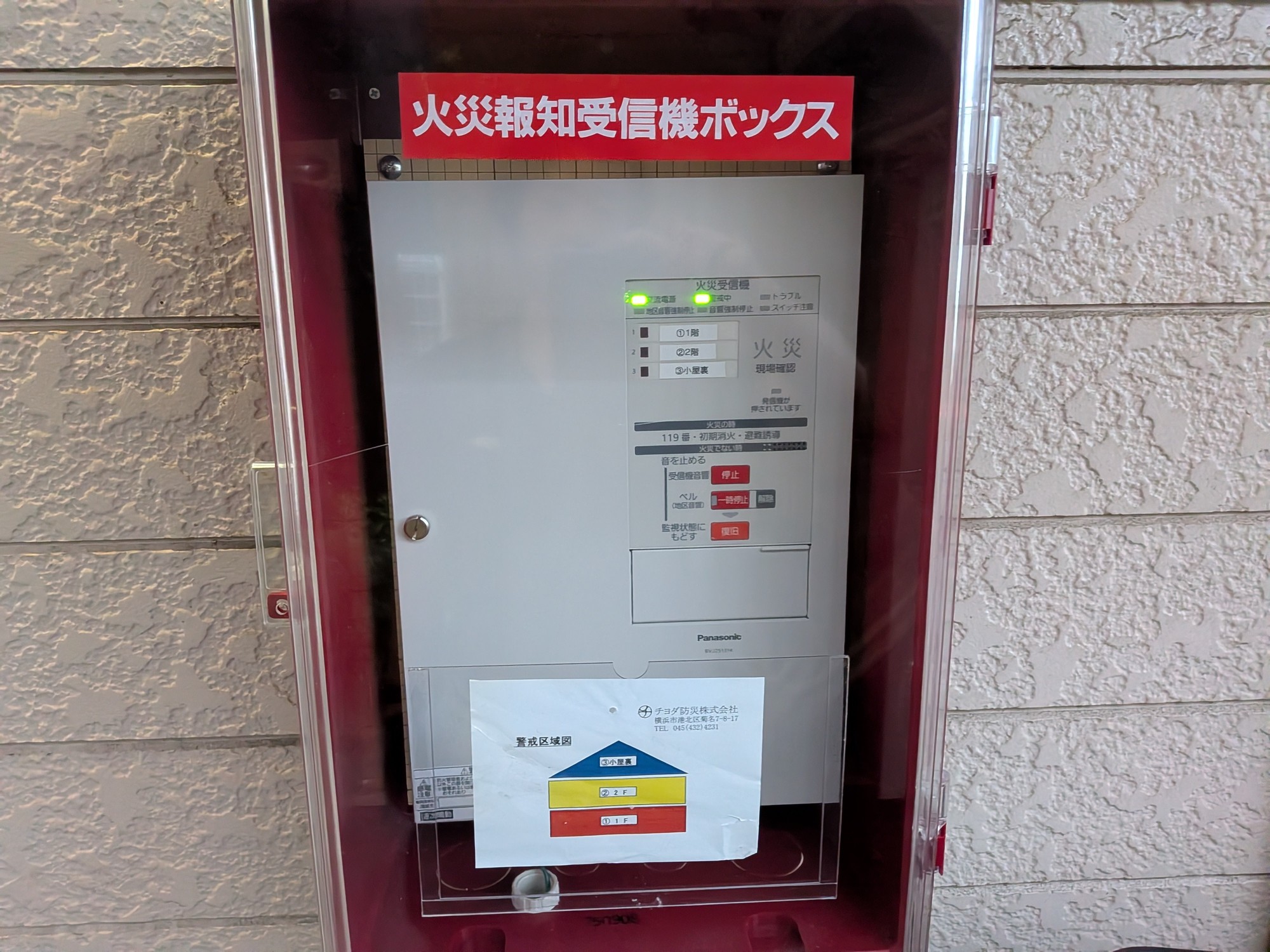 交換後の火災受信機。赤い防雨型格納箱に収められたパナソニック製P型2級受信機と、1階・2階・小屋裏の3区域を示す警戒区域図