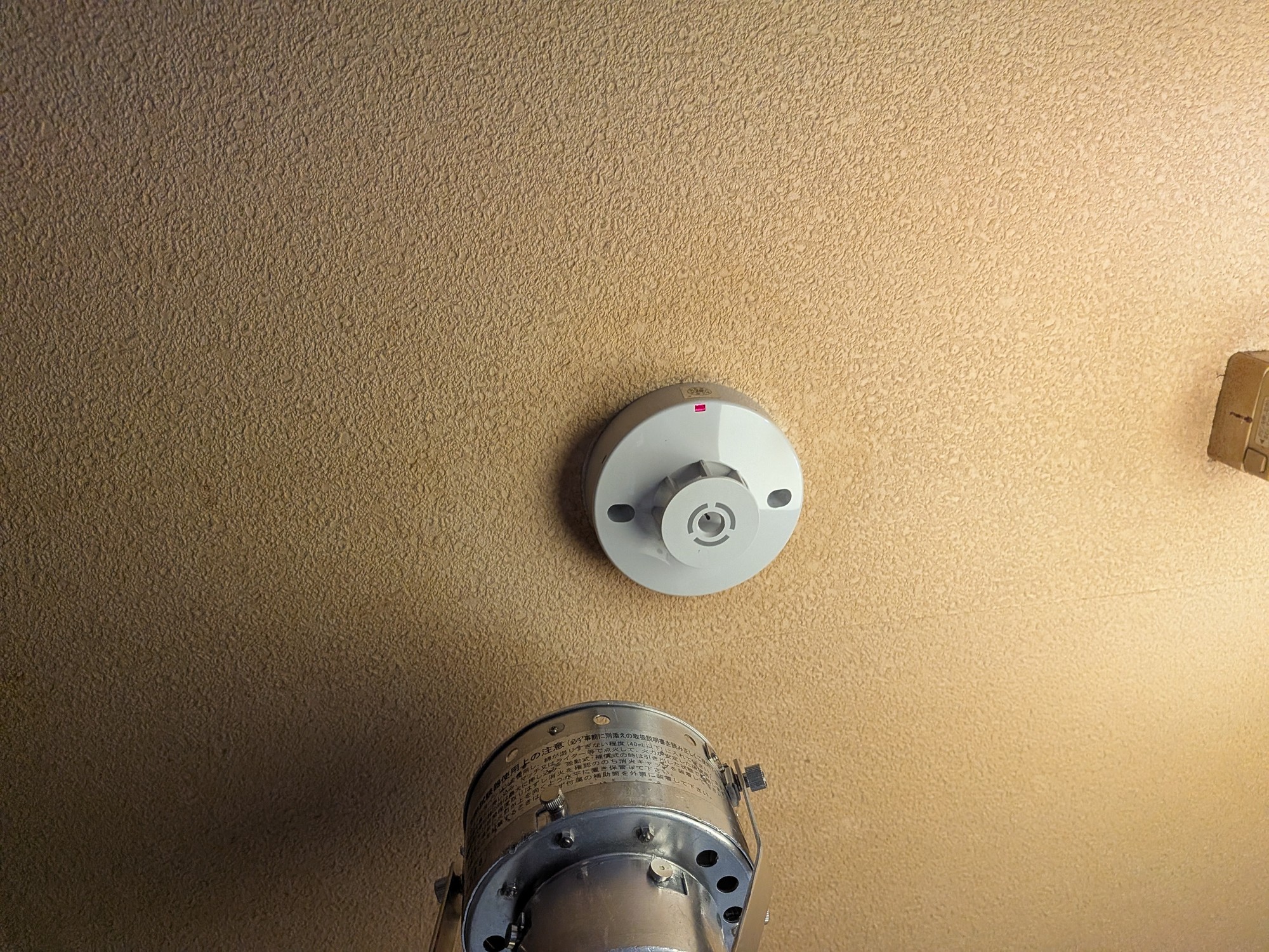 天井に取り付けた交換後の感知器と、その下にかざした加熱試験器