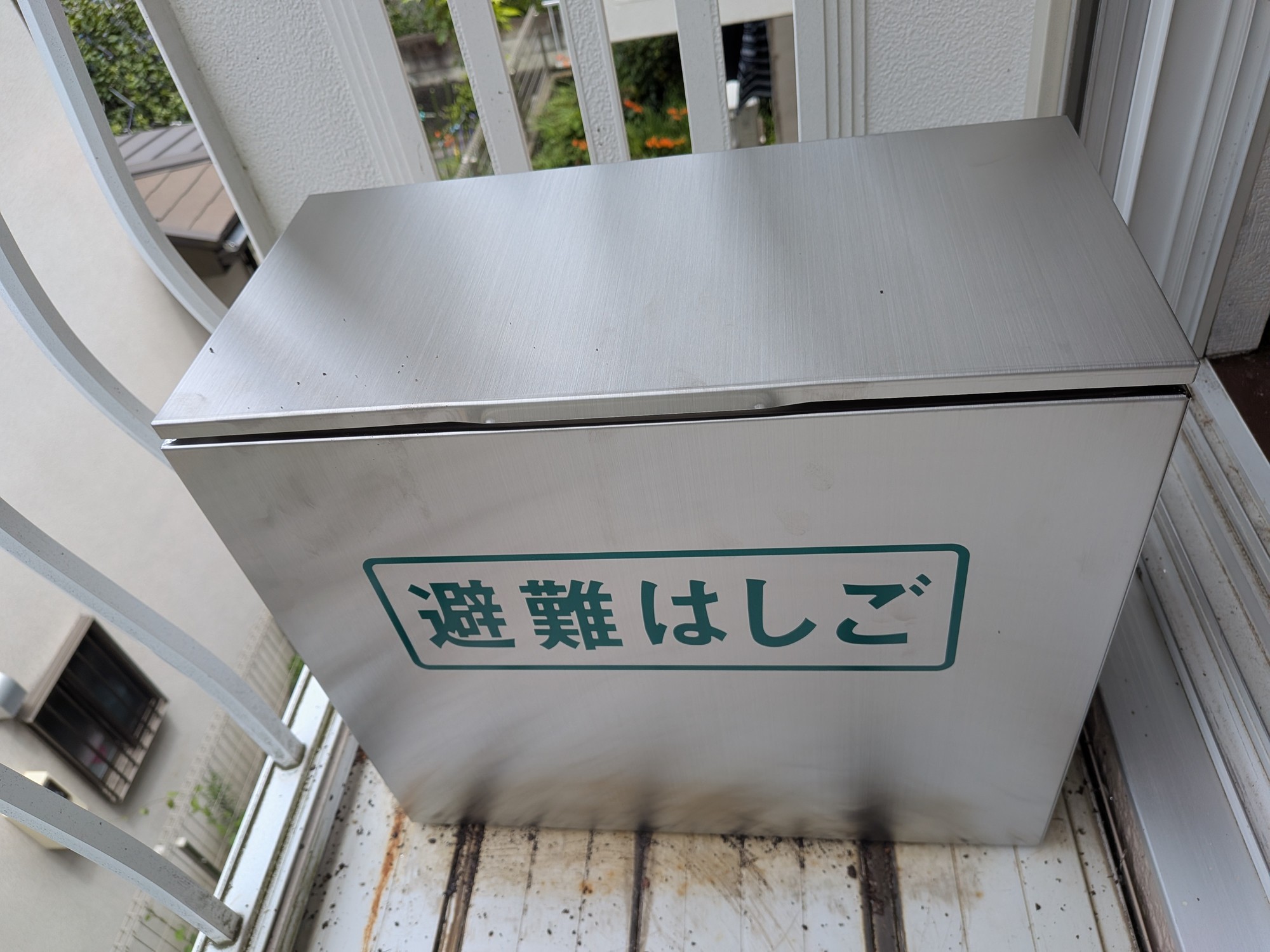 交換後のステンレス製避難はしご格納箱。バルコニーに設置され、緑色で「避難はしご」と表示されている