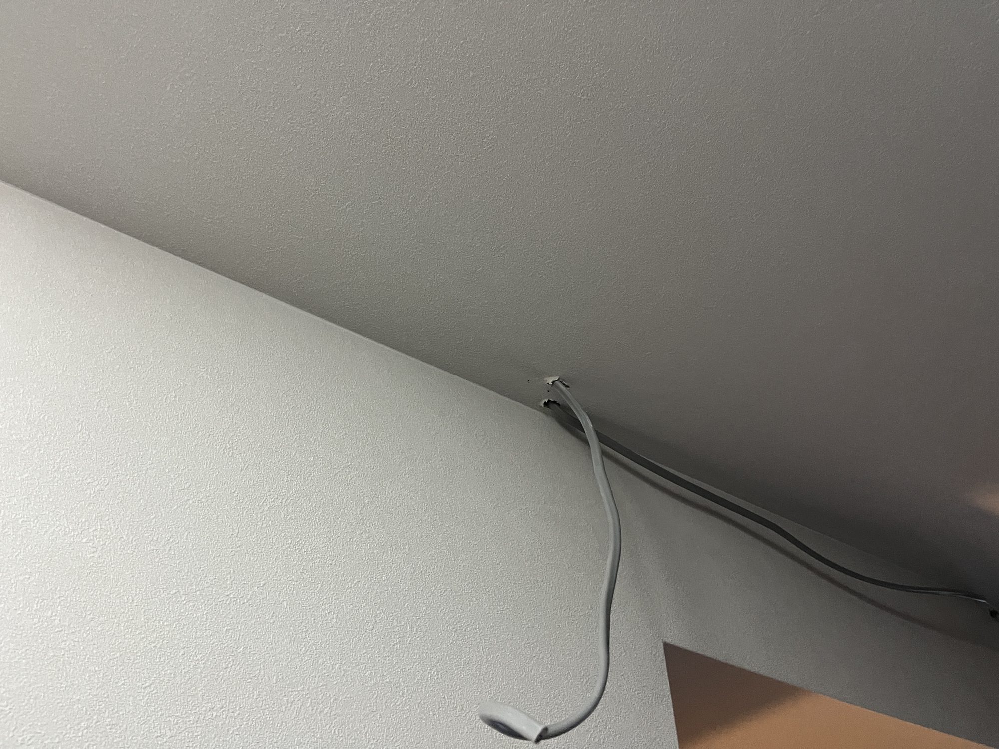 壁と天井の取り合いから引き出した電源ケーブル。モールで保護する前の状態