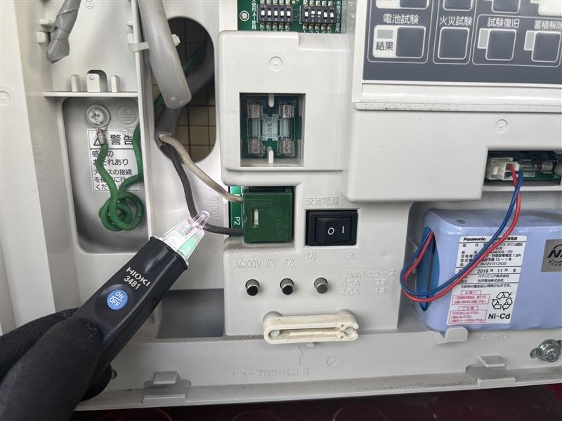 検電器で受信機の交流電源端子を確認し、電源が来ていないことを確かめている様子