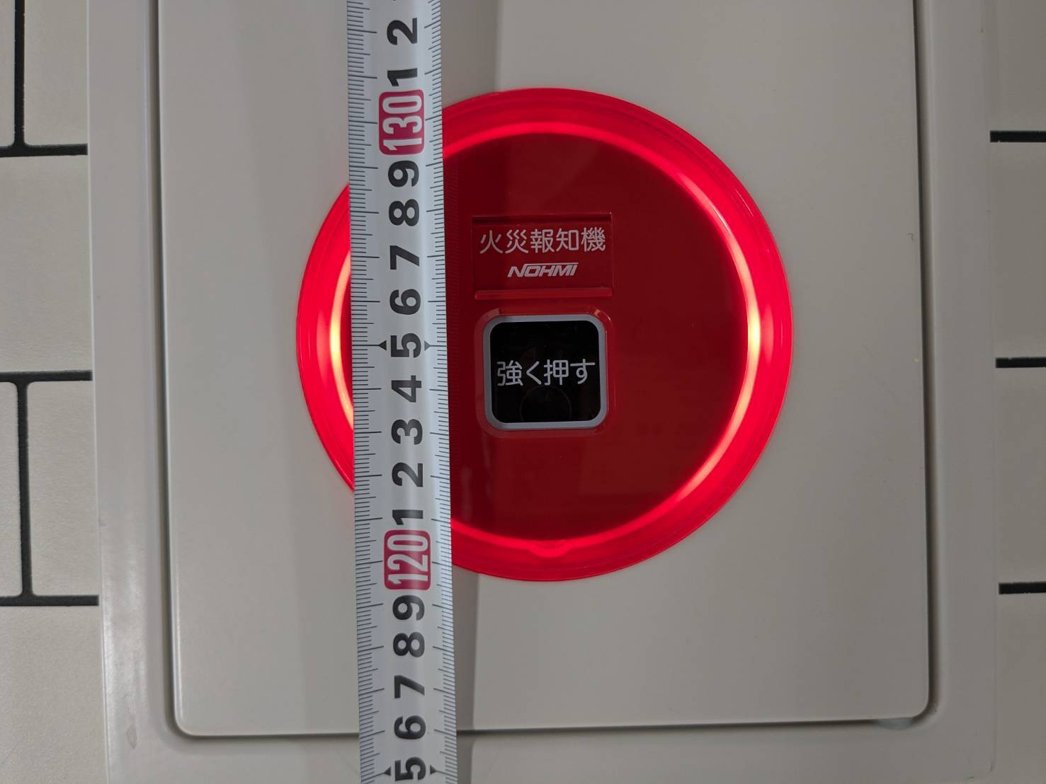 発信機の押しボタンの高さをメジャーで計測。床面から約1.25mで基準内