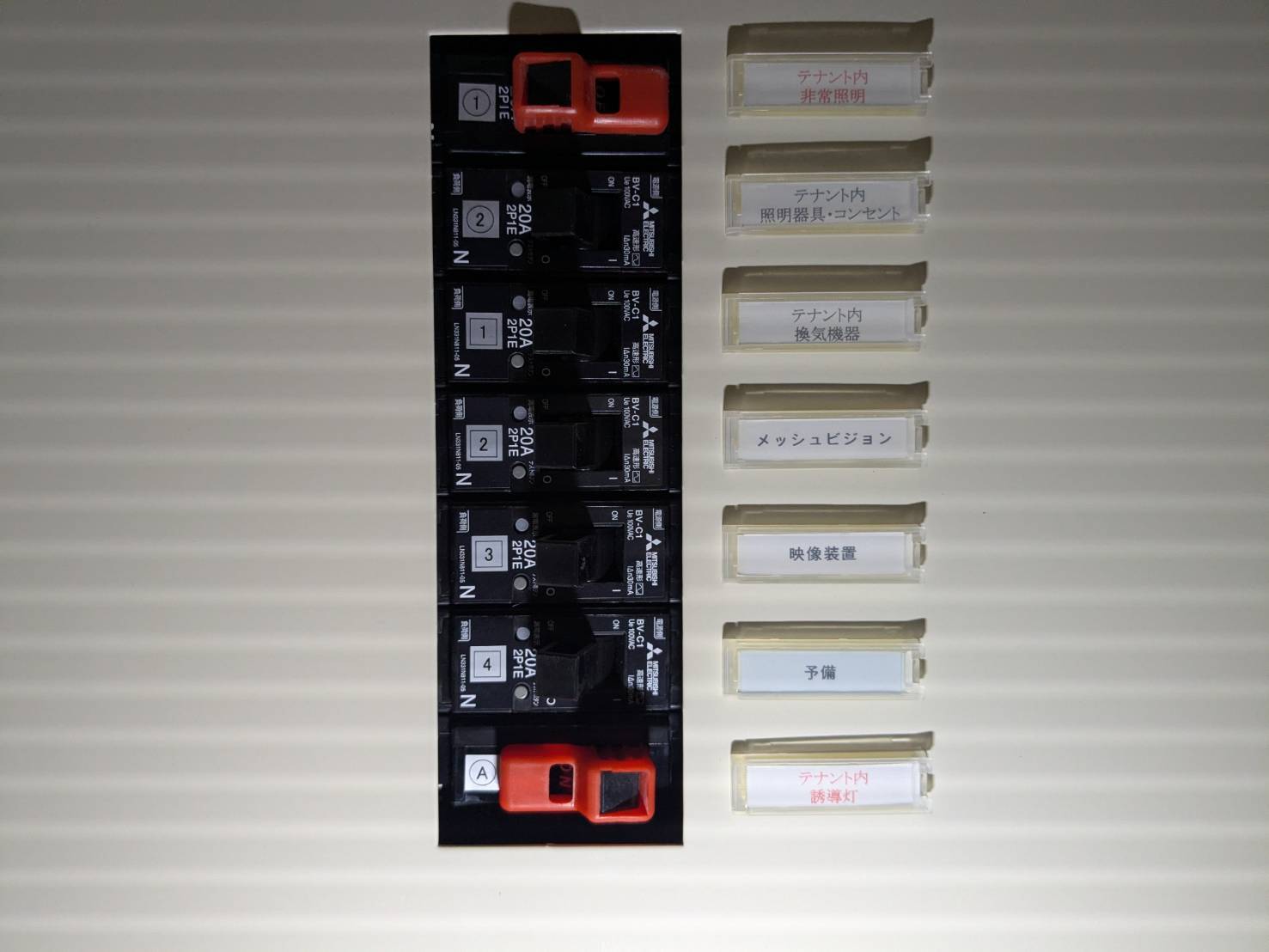 テナントの分電盤。誘導灯と非常照明のブレーカーに赤字の回路名札を付けている
