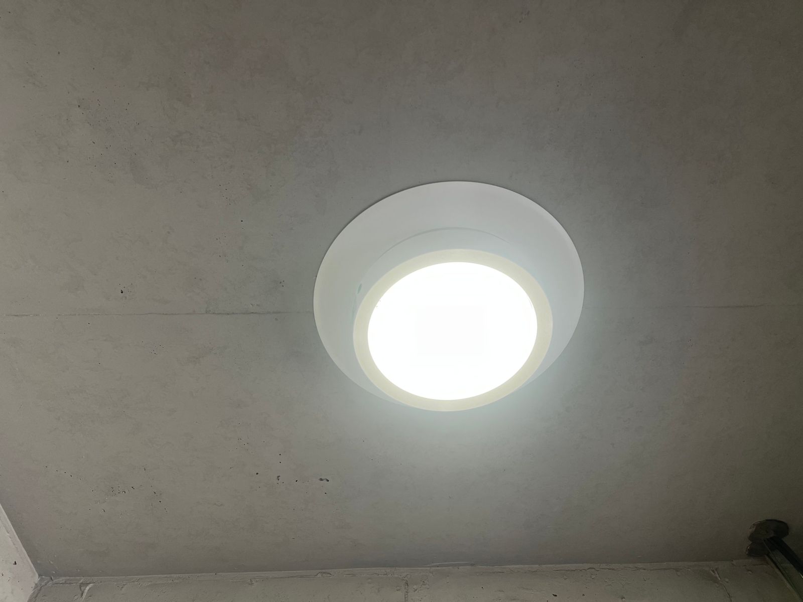 交換後のLED非常灯。同じコンクリート天井に新しい丸型のLED器具が取り付けられ、白く明るく点灯している。