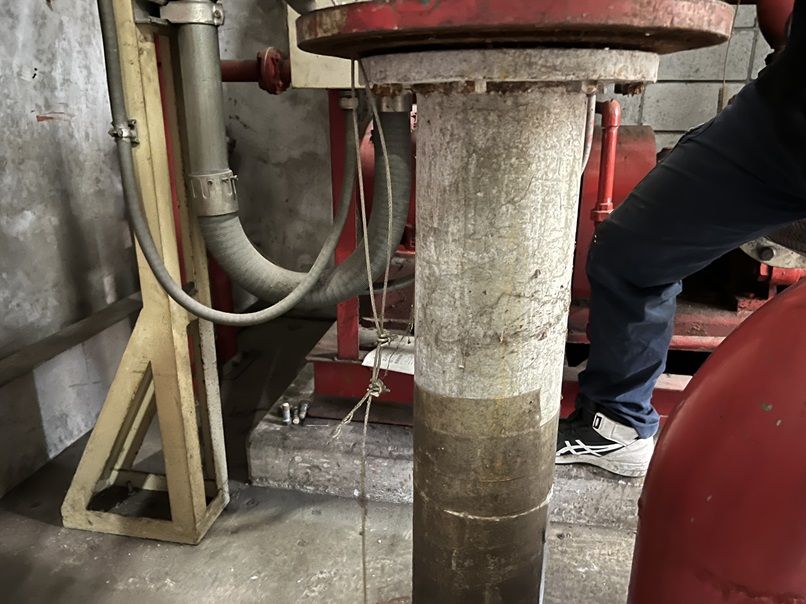 交換前のスプリンクラーポンプの吸水管。床の貫通部から立ち上がる配管の下側が、水に浸かっていた部分だけ黒く変色している