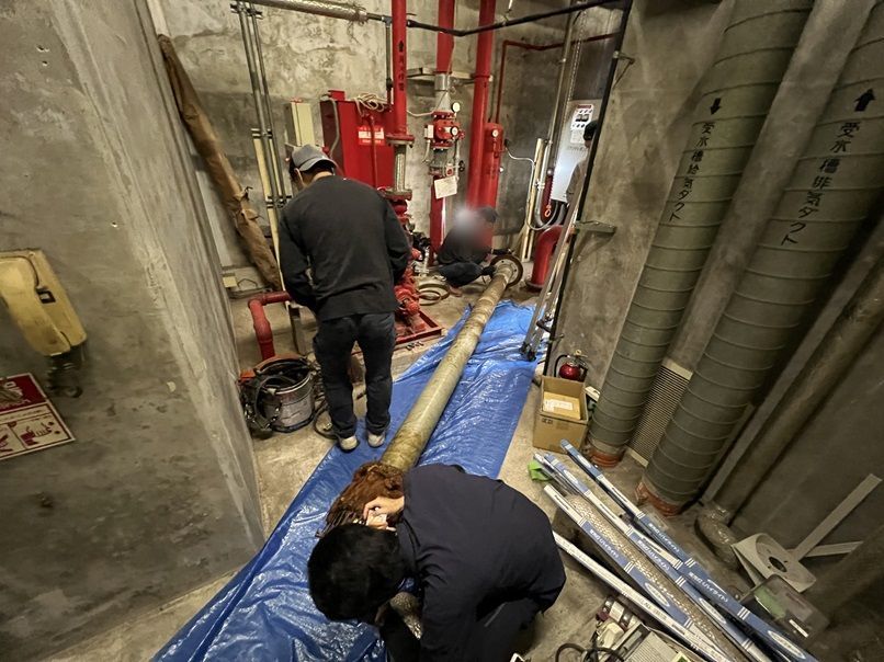 取り外した古い吸水管を養生シートの上に横たえて、作業員が状態を確認している