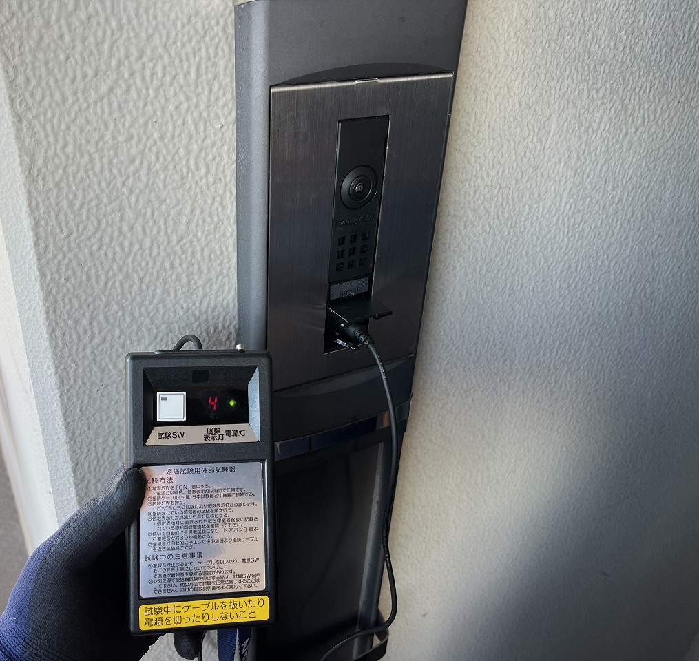 遠隔試験用外部試験器を玄関子機に接続し、住戸内の感知器を試験する様子