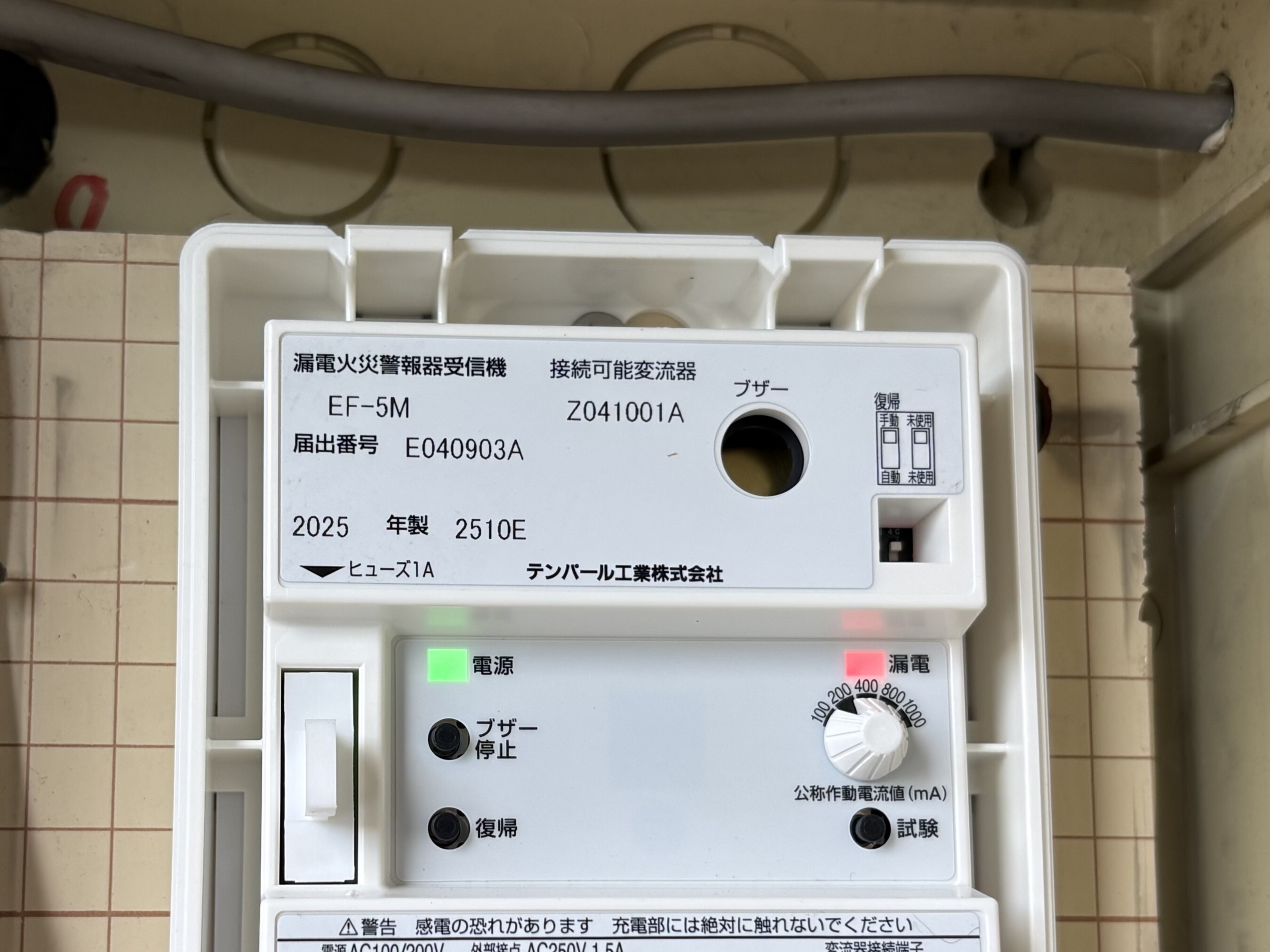 交換後の漏電火災警報器受信機テンパール工業EF-5Mのカバー内部。電源の緑ランプと漏電の赤ランプが点灯、公称作動電流値ダイヤル、ブザー停止・復帰・試験ボタン