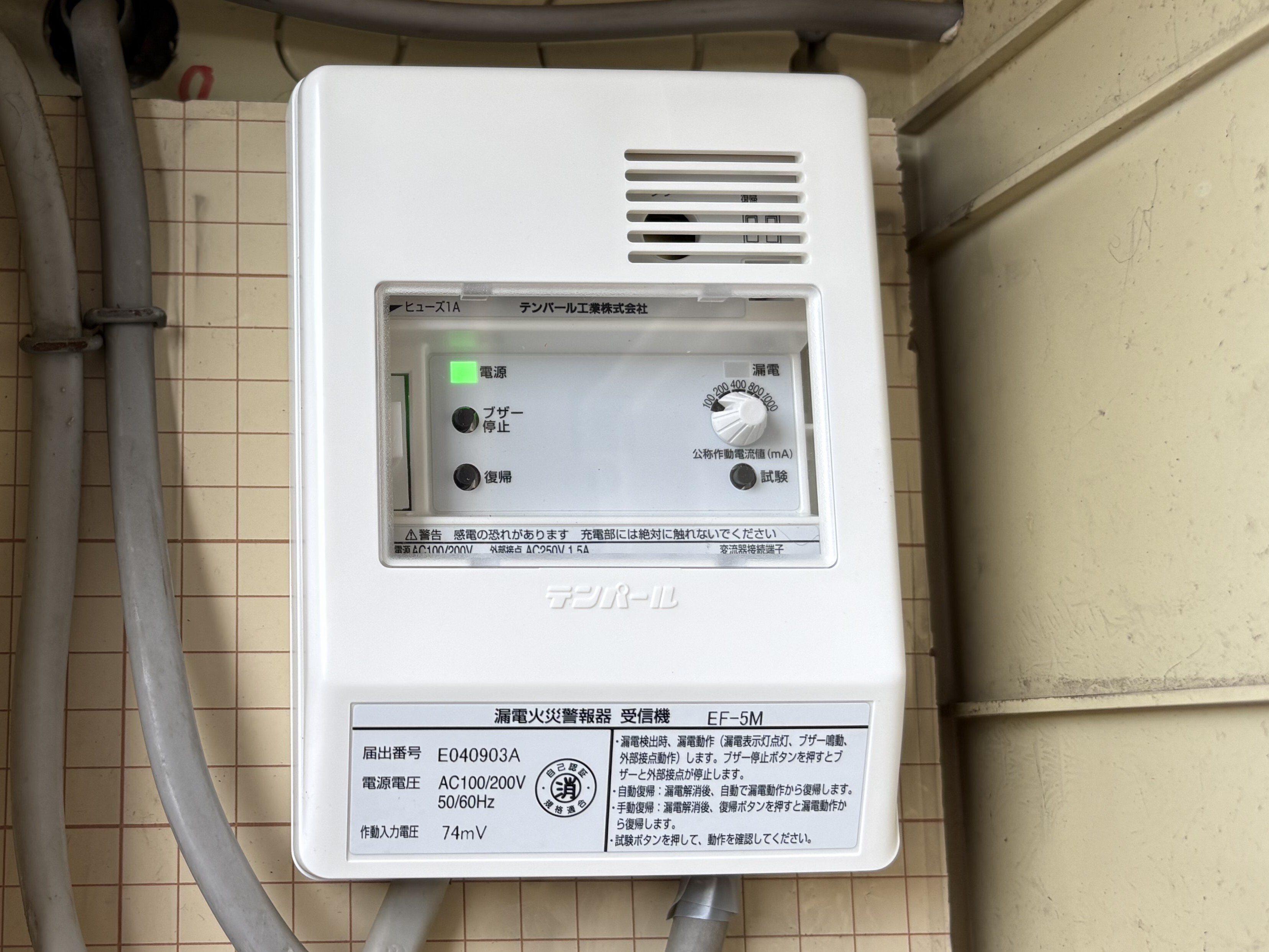 交換後の漏電火災警報器受信機EF-5Mの完成外観。白いカバーの窓から電源ランプが点灯、下部に届出番号E040903Aと取扱説明のラベル