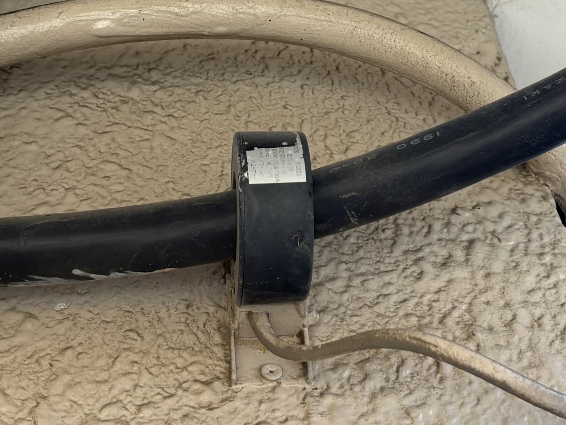 交換前の漏電火災警報器の変流器。屋外の引込線にリング状の変流器が取り付けられ、銘板は退色している
