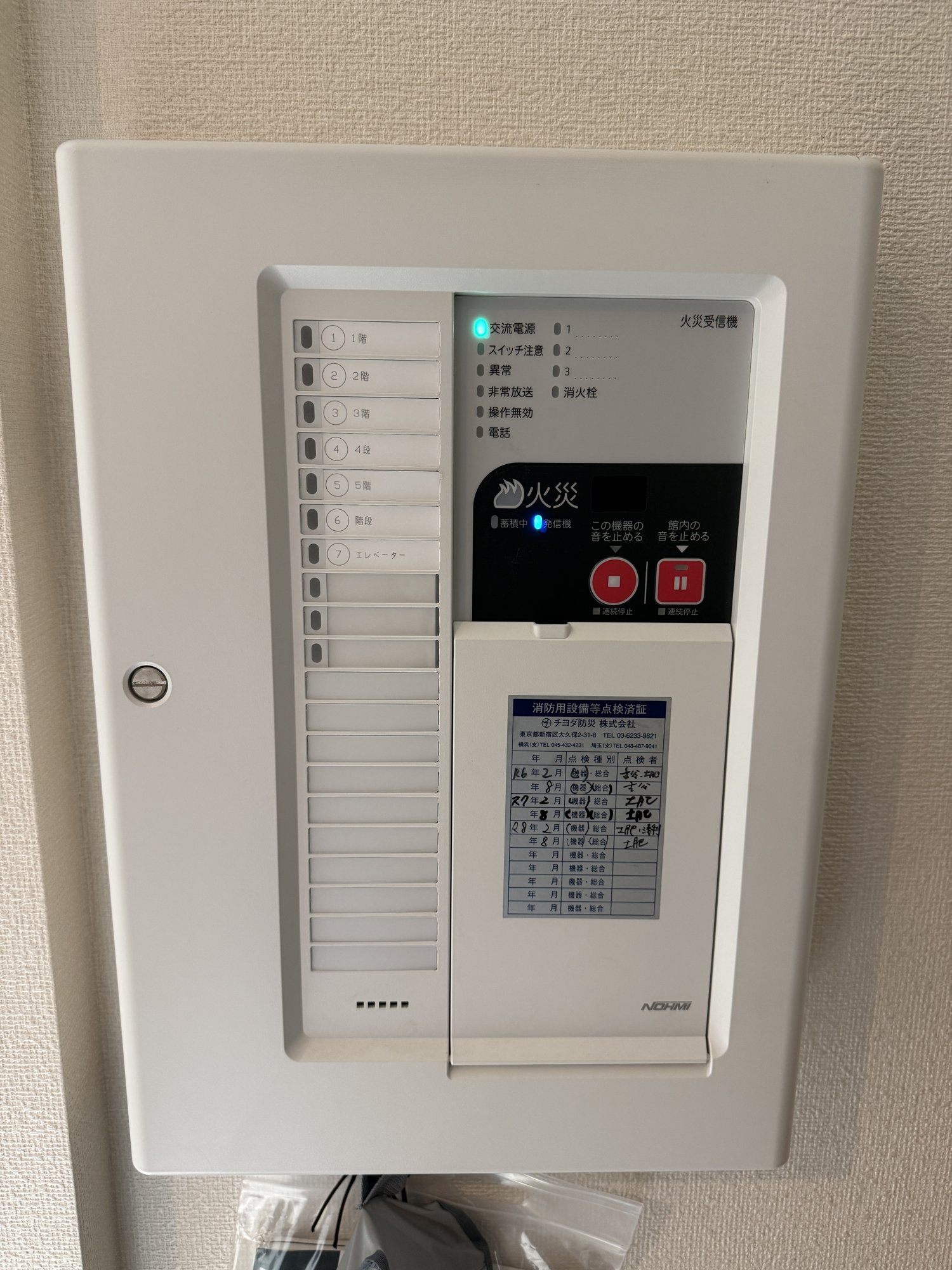 能美防災P型1級受信機の正面写真。扉を閉めた状態で、左に地区表示の窓、右に火災表示と赤いボタン2つがある